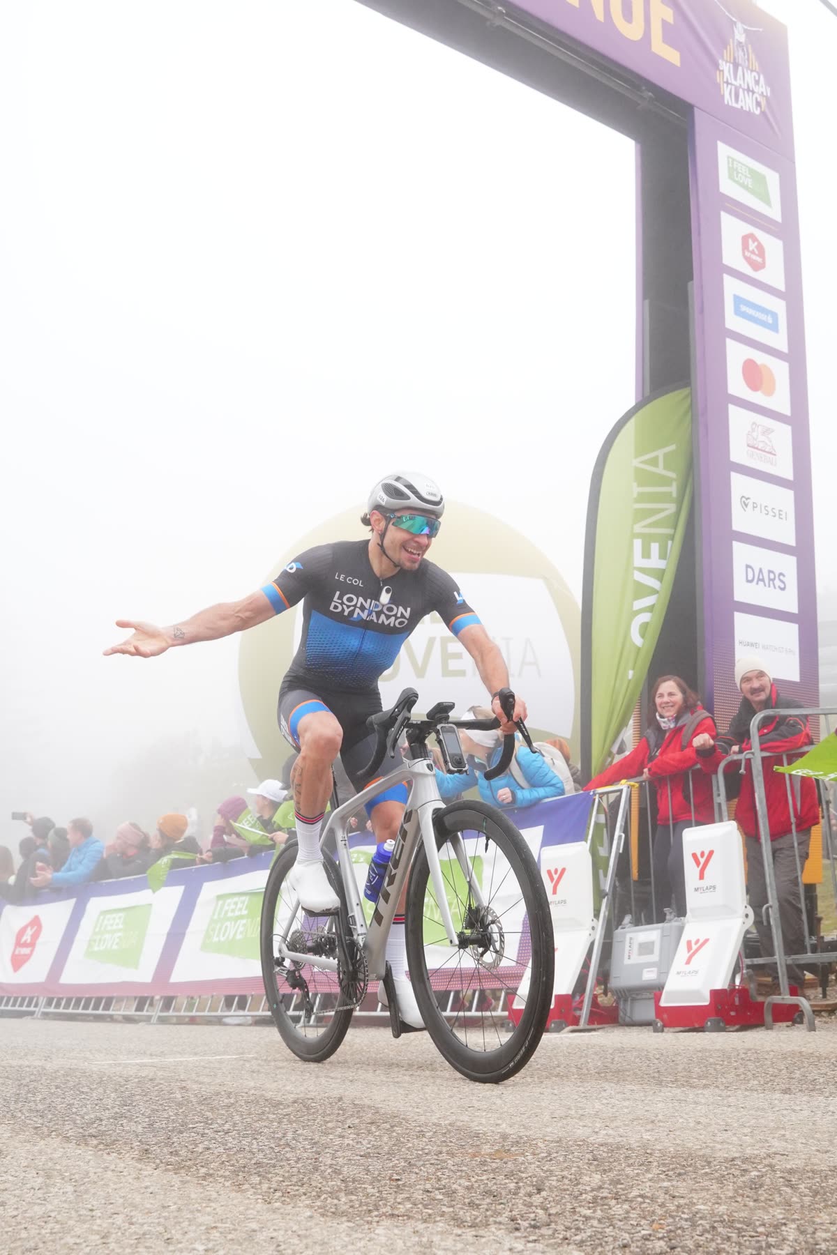 Rodrigo crossing a finish line with one arm out, crowd behind the barriers